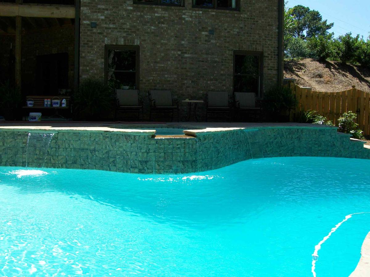 Tiled raised spa wall with sheer waterfalls spilling into a freeform pool