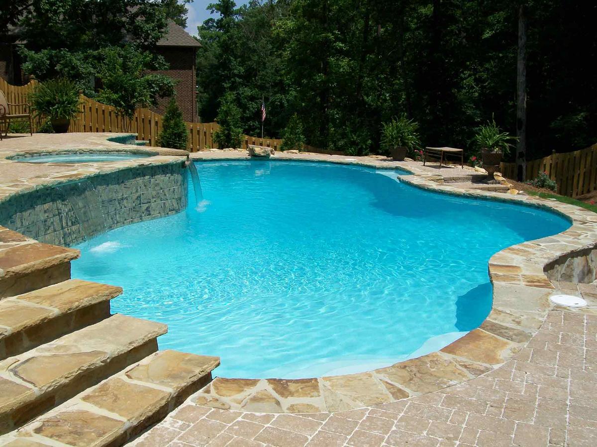 Freeform pool with spa spillover, flagstone steps and coping beside wooded fence line