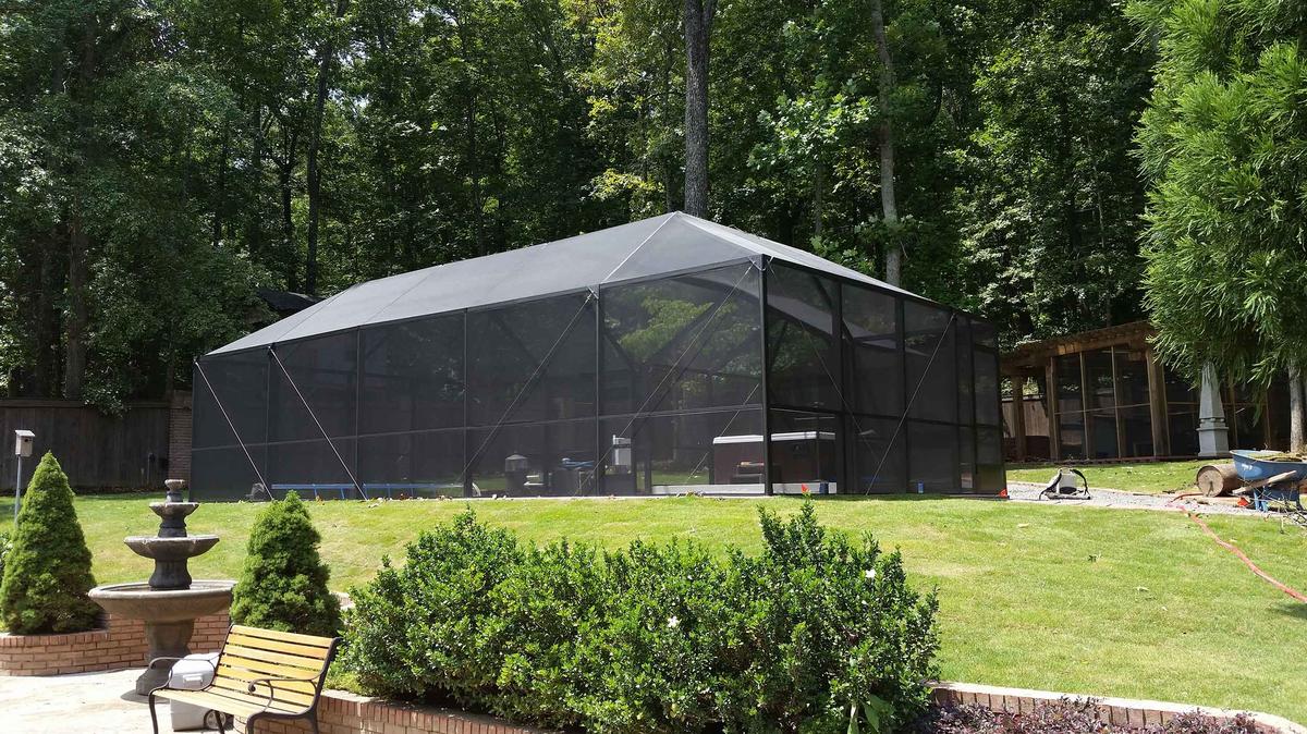 Screened pool enclosure on a lawn surrounded by tall trees
