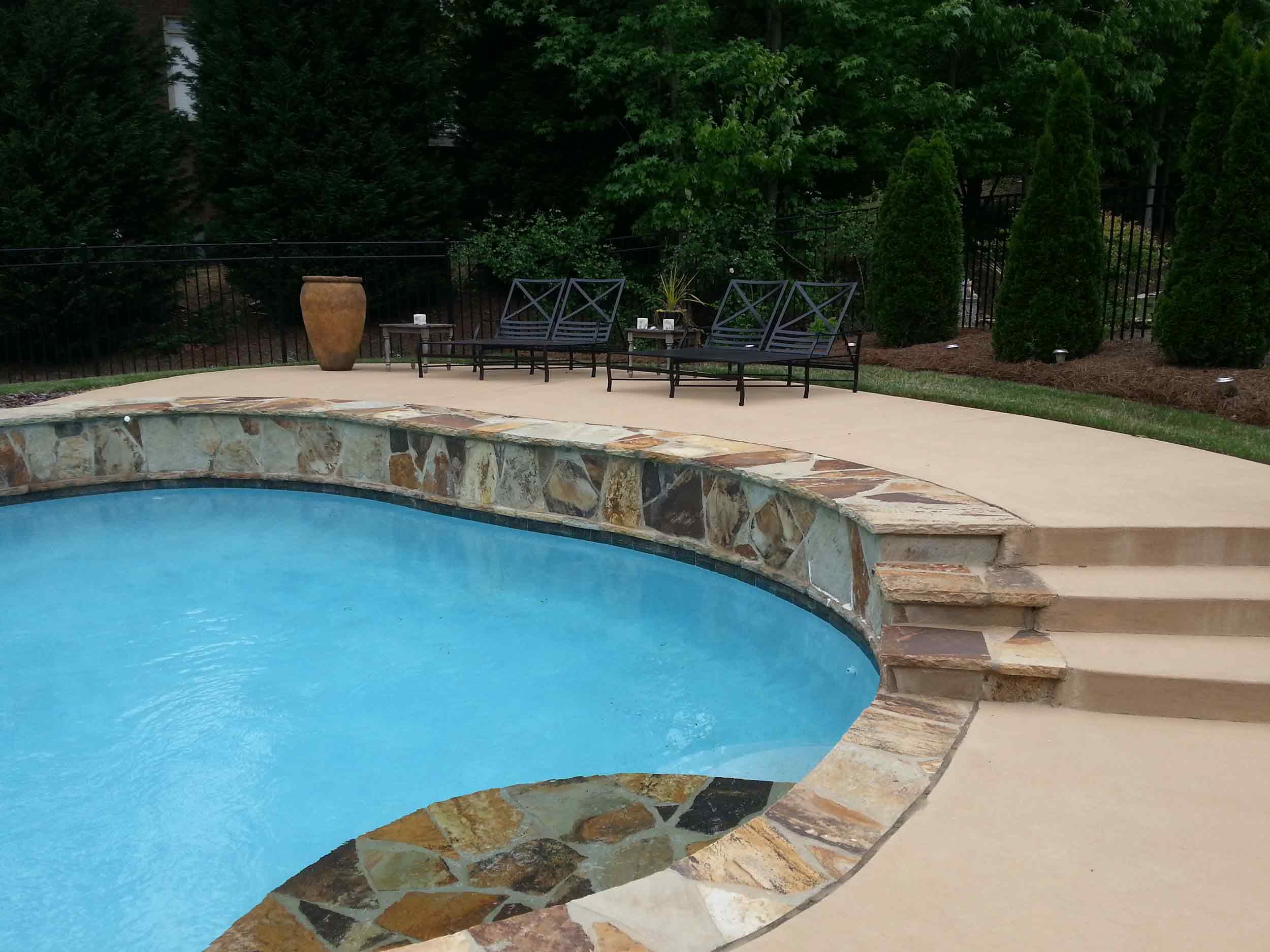 Freeform pool with raised flagstone wall, stone steps and concrete deck
