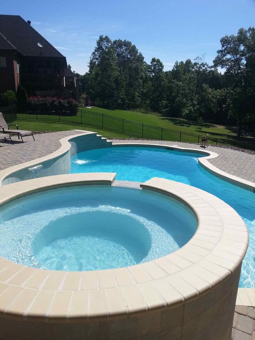 Freeform pool with raised round spa, sheer descent waterfalls and paver deck