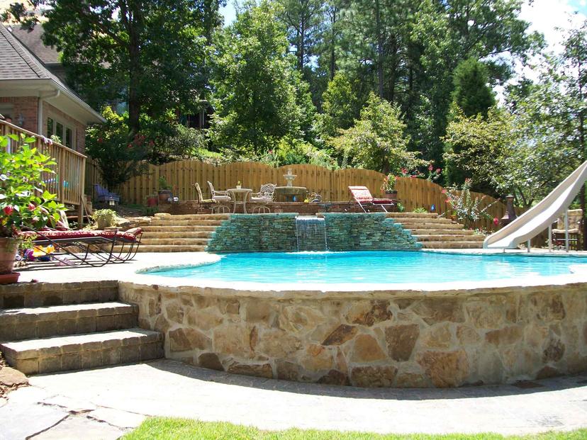 Pool with stone-faced raised wall, spa waterfall, wide stone steps and slide