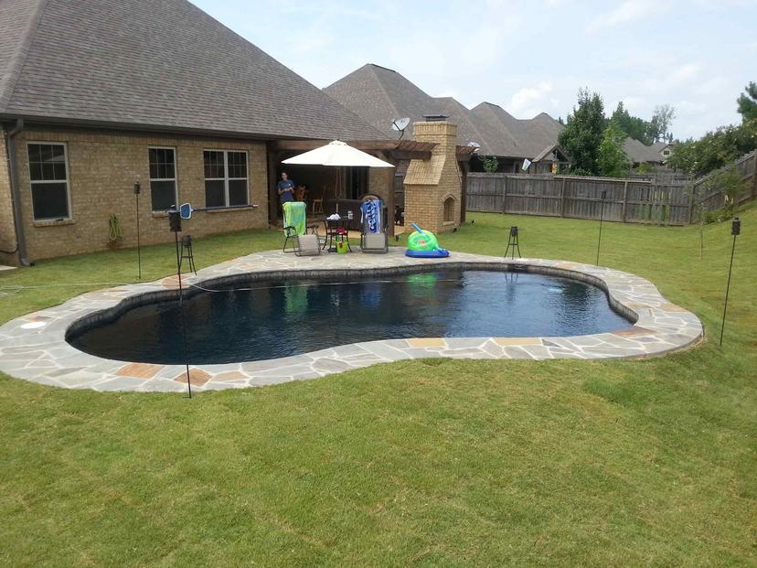 Dark-finish freeform pool with flagstone deck in open suburban lawn