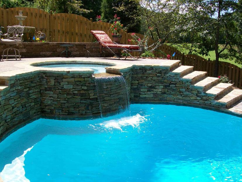 Stacked stone spa waterfall pouring into pool beside stone steps to patio