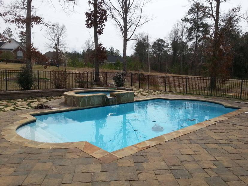 Roman-end pool with raised stone spa spillover on paver deck, fenced yard